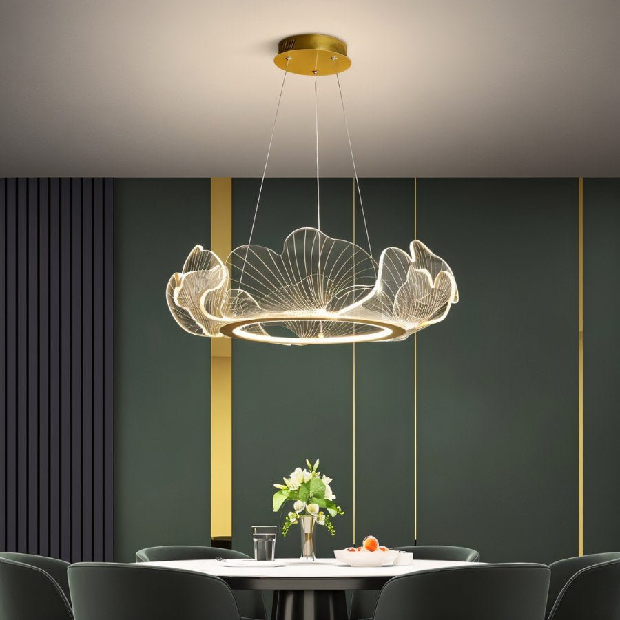 Clérachic leaf chandelier in clear acrylic with a glowing gold ring, hung low above a white dining table and green chairs.