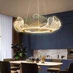 Clérachic lit leaf chandelier with a gold ring over a dining table in a navy kitchen with a marble splashback.