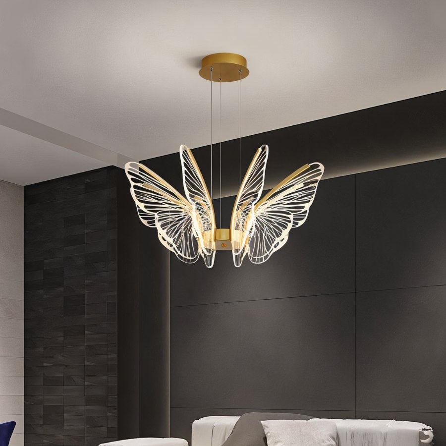 Clérachic gold butterfly chandelier with clear acrylic wings, above a pale sofa in front of dark stone-effect panels.