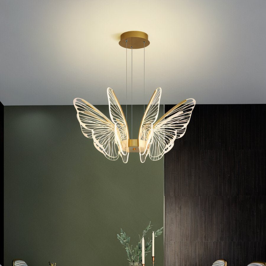 Clérachic butterfly chandelier in gold and clear acrylic, hung against a green wall with a ribbed dark panel beside it.