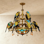 Clérachic two-tier stained-glass style chandelier with twelve glass parrots on gilt-brass arms, hung from a chain over limewash.