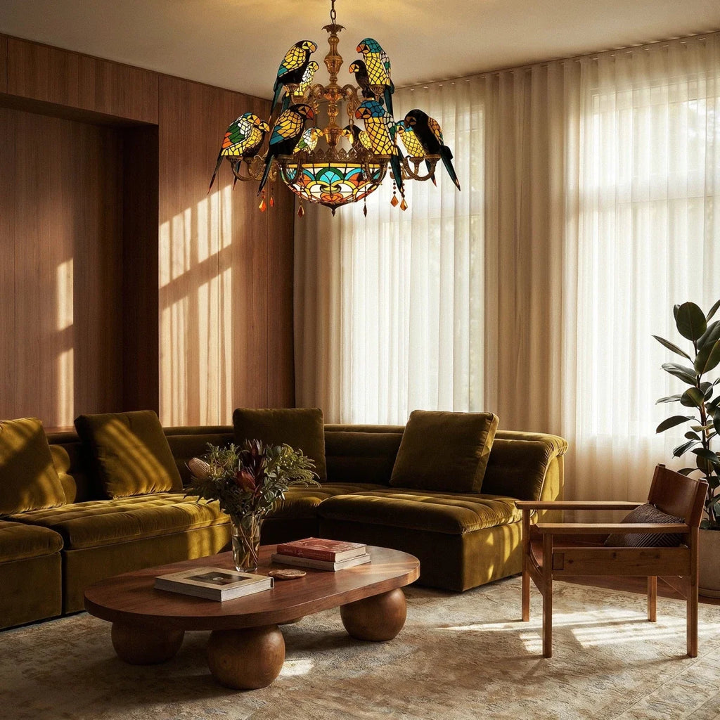 Clérachic twelve-parrot stained-glass style chandelier over a low wooden coffee table and an olive velvet sofa.