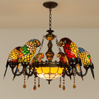 Clérachic six-parrot chandelier in red, green and yellow glass with a plain amber bowl and chain, against a pale wall.