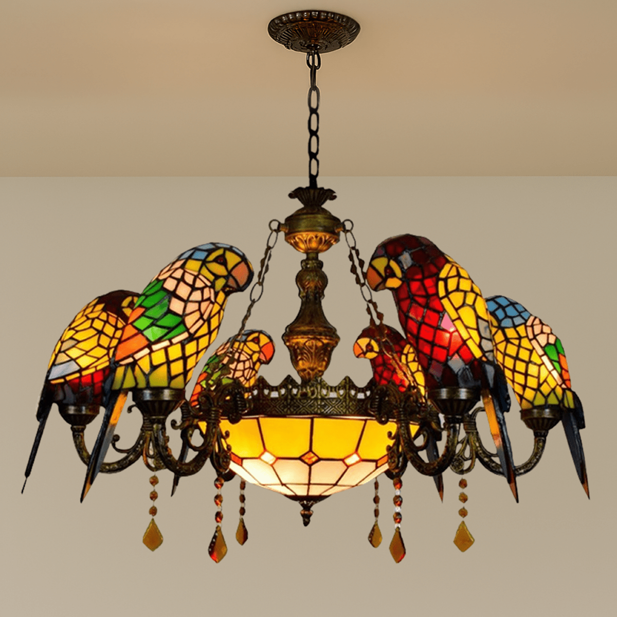 Clérachic six-parrot chandelier in red, green and yellow glass with a plain amber bowl and chain, against a pale wall.