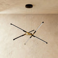 Clérachic starburst chandelier with six slim LED rods in black and brushed gold, hung on three cables against plaster.
