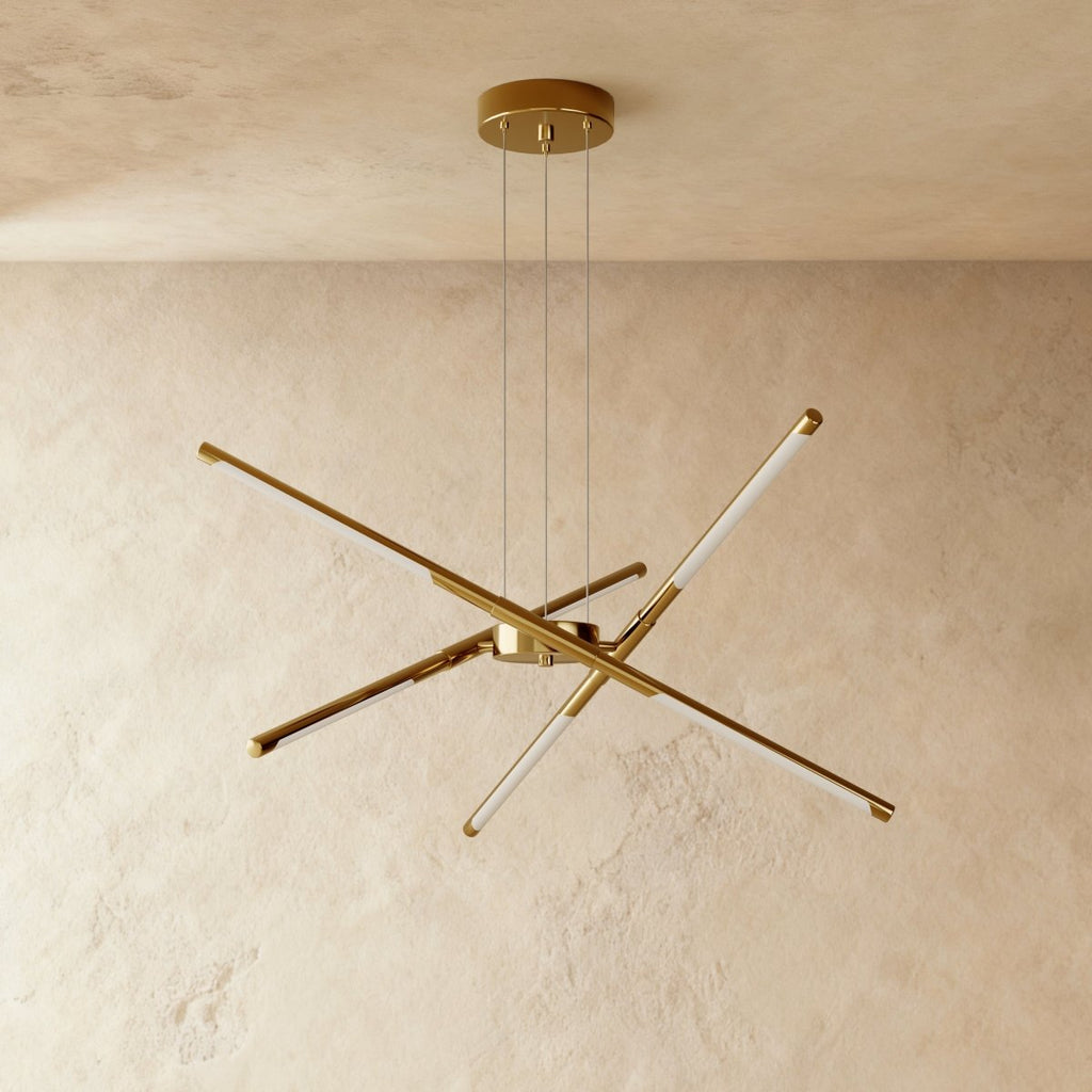 Clérachic starburst chandelier with six slim LED rods in all-gold metal, hung on three cables against limewashed plaster.