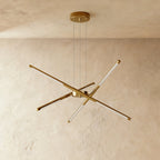 Clérachic starburst chandelier with six slim LED rods in all-gold metal, hung on three cables against limewashed plaster.