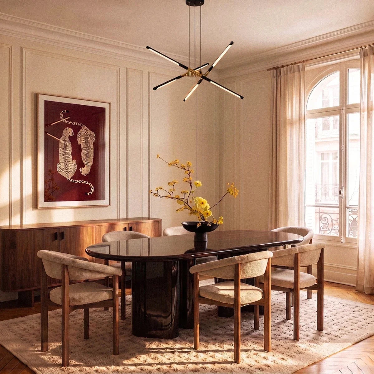 Clérachic black and gold starburst chandelier over an oval dark dining table, with a window and moulded walls behind.