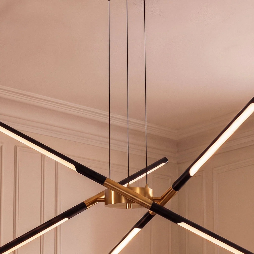 Close view of the Clérachic chandelier hub in brushed gold, with black rods and lit LED strips and three black cables.