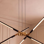 Close view of the Clérachic chandelier hub in brushed gold, with black rods and lit LED strips and three black cables.