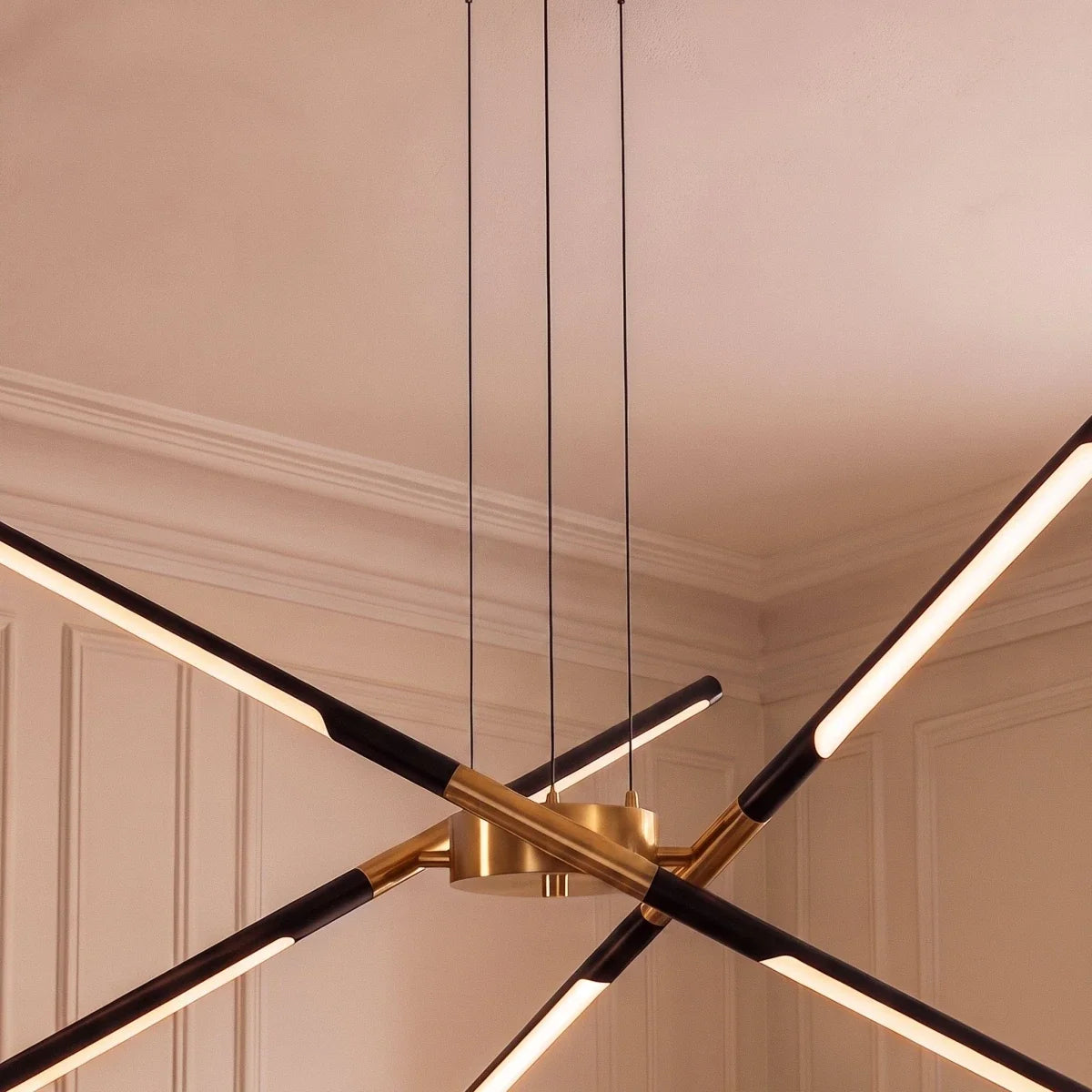 Close view of the Clérachic chandelier hub in brushed gold, with black rods and lit LED strips and three black cables.