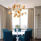 Gold trumpet-head Clérachic chandelier above a round white table and teal leather chairs, in front of a tall city-view window.