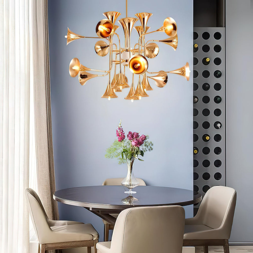 A Clérachic chandelier with gold horn-shaped shades hangs above a round dark table with a vase of pink flowers, against a blue wall.