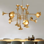 Large gold Clérachic chandelier with trumpet heads on branching arms, hung in front of a pale wall above a long dining table.