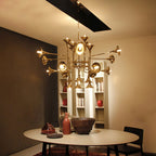 Warmly lit Clérachic chandelier with gold horn shades over a round dining table, with open shelving and ceramics behind.