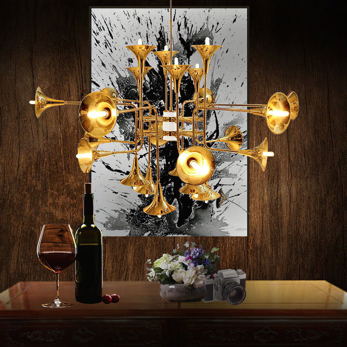 Gold Clérachic chandelier with trumpet heads against a dark wood wall and a black-and-white painting, above a table with wine.