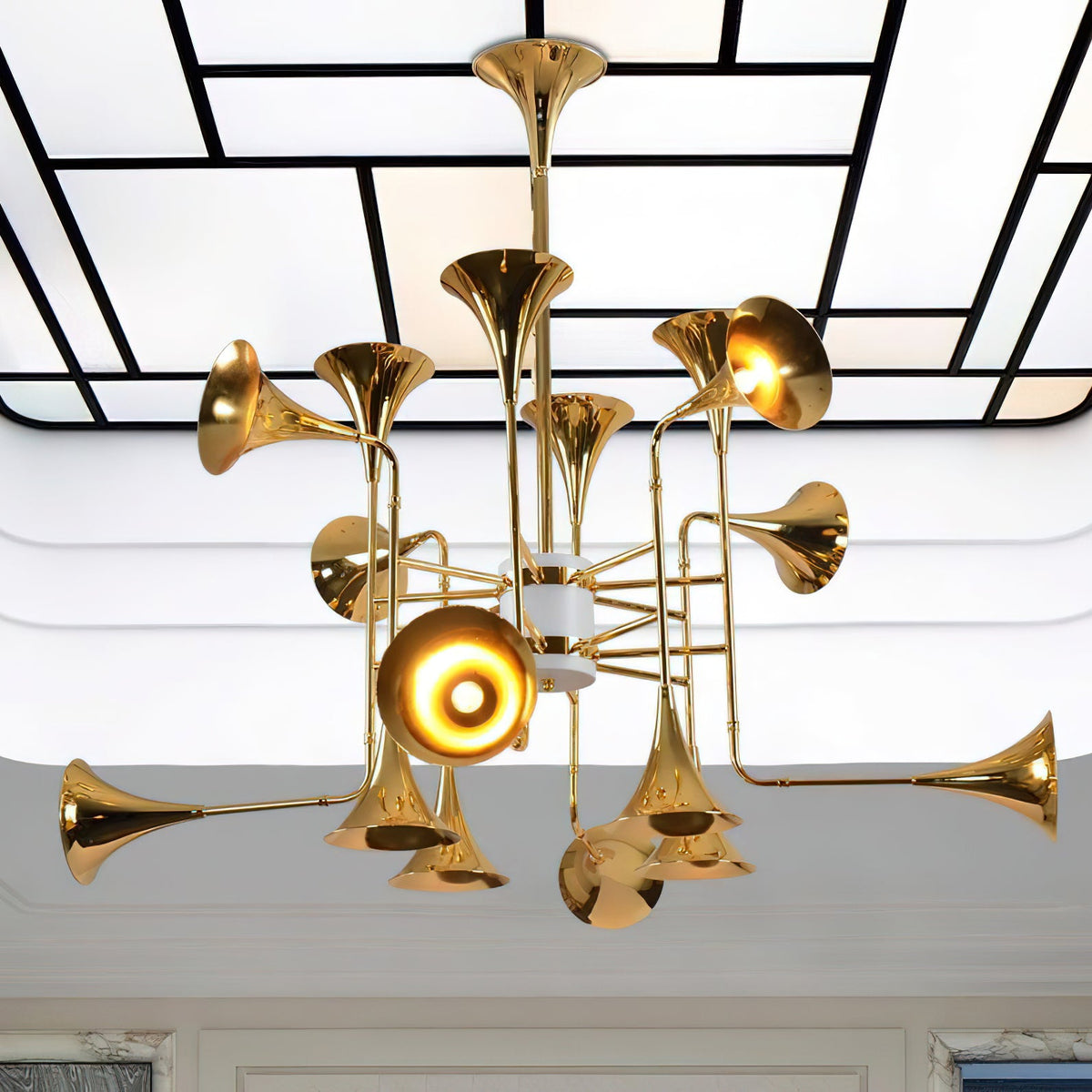 Looking up at the gold horn-shaped heads of this Clérachic chandelier, set against a ceiling of white panels and black lines.