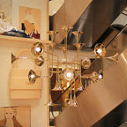 A Clérachic chandelier with gold trumpet heads hangs in a shop stairwell, with fashion displays and an escalator behind.
