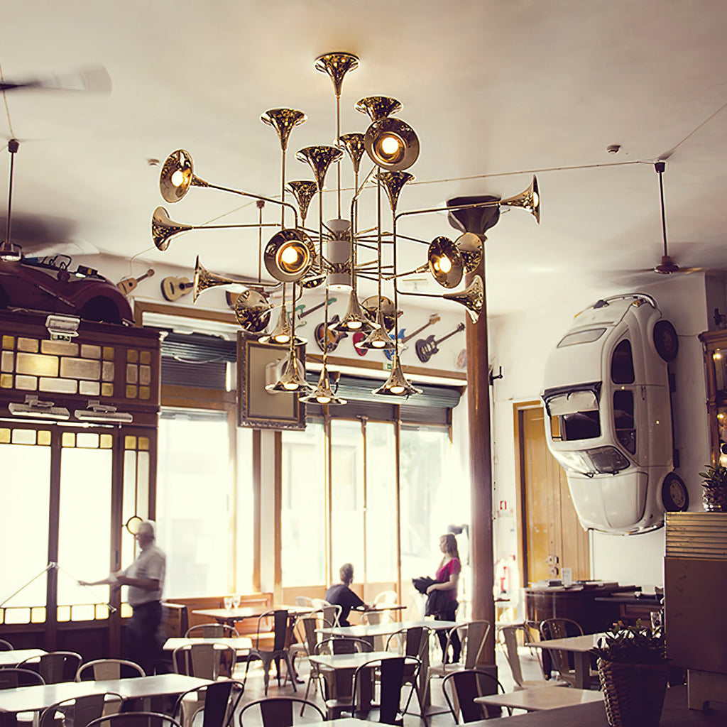 Gold Clérachic chandelier hung in a cafe with big windows, wall decor and round tables, with people at the tables below.