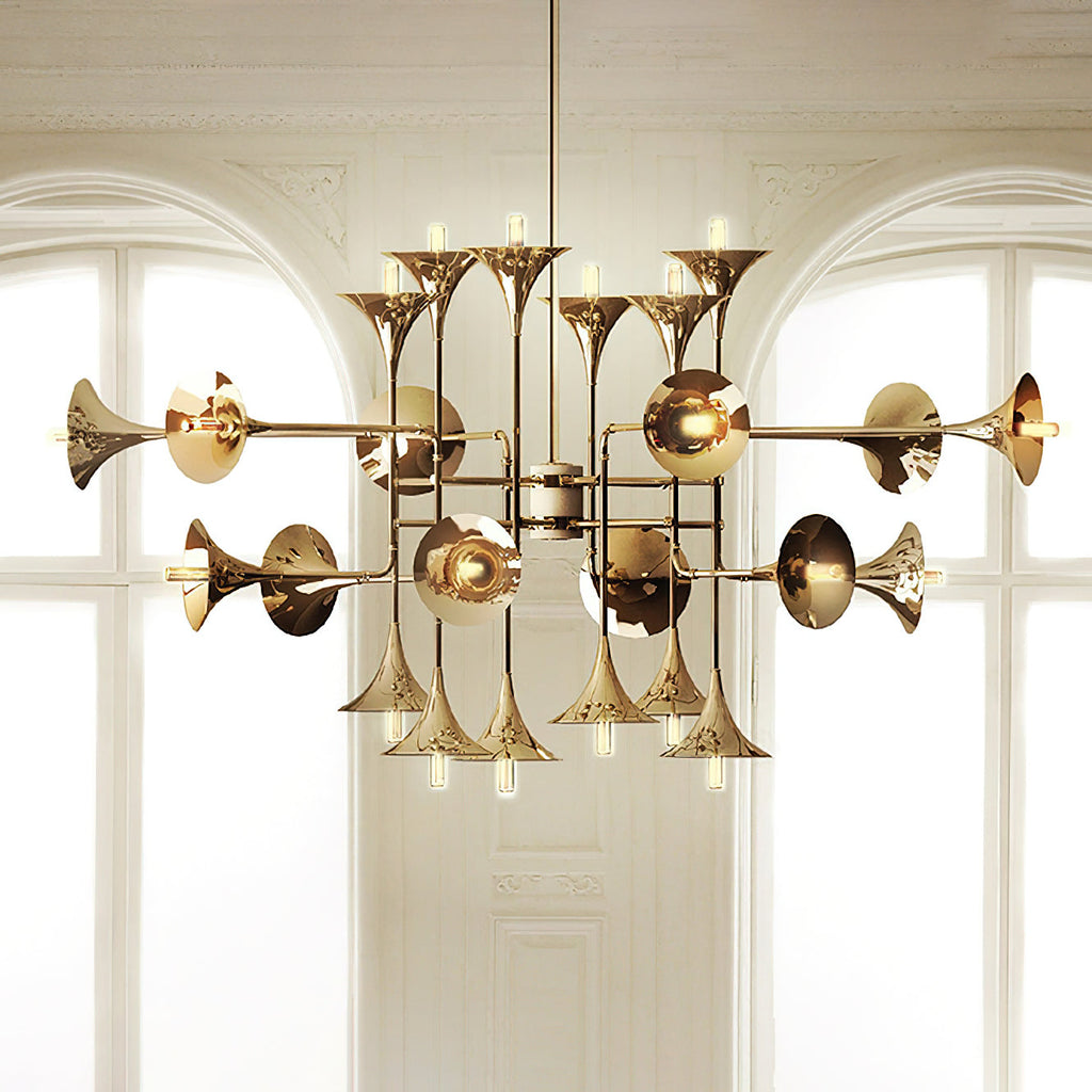 Gold Clérachic chandelier with horn-shaped shades, hung in front of two tall arched windows with white framing.