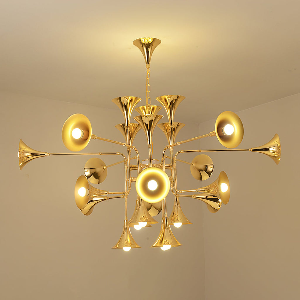 Lit gold Clérachic chandelier in a plain cream room, its trumpet heads glowing around the central stem.