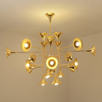 Lit gold Clérachic chandelier in a plain cream room, its trumpet heads glowing around the central stem.