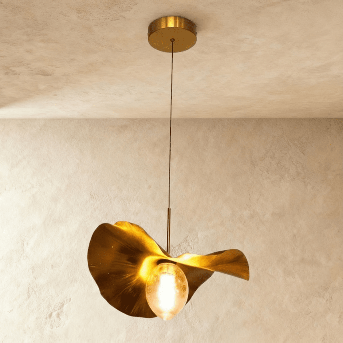Clérachic pendant with a wavy gold leaf-shaped metal shade and a lit amber glass bulb, hung from a brass ceiling canopy.
