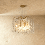 Clérachic gold chandelier with curved arms and cascading crystal drops, lit and hung from a round canopy in a studio setting
