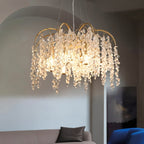 Clérachic gold crystal chandelier glowing over a sofa in a grey room, its drops catching the warm light from six bulbs