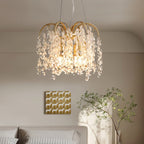 Clérachic gold chandelier with frosted and clear crystal drops lit above a sofa in a pale bedroom with a plant and framed art