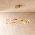 Clérachic twisted gold ring chandelier of clear crystal bars, hung on fine cables from a gold ceiling plate against limewashed plaster.