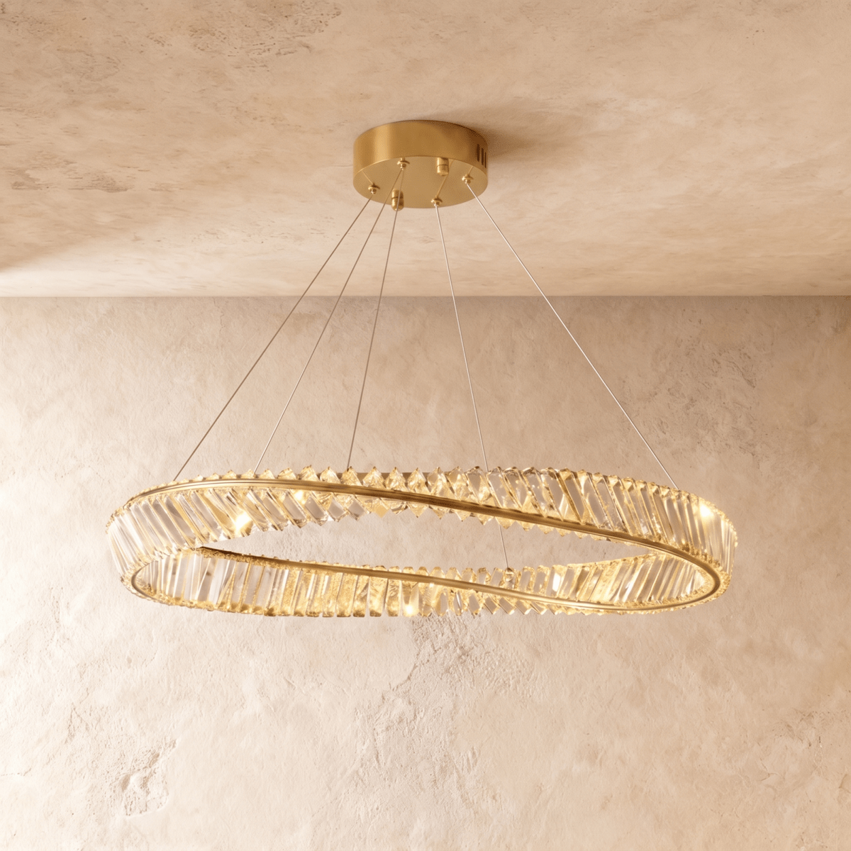 Clérachic mid-size twisted gold ring chandelier of clear crystal bars on slim cables, photographed against textured plaster walls.