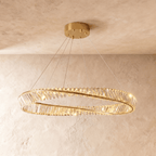 Clérachic large twisted gold ring chandelier set with crystal bars, hanging below a gold canopy in front of a plaster wall.