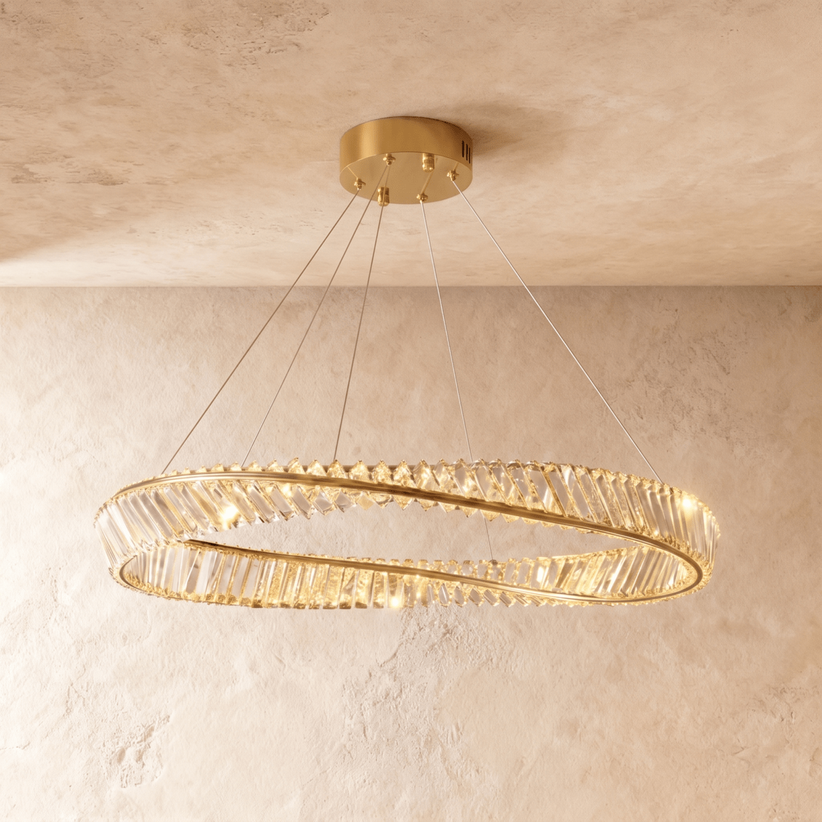 Clérachic large twisted gold ring chandelier set with crystal bars, hanging below a gold canopy in front of a plaster wall.