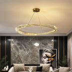 Clérachic flat gold crystal ring chandelier glowing warm above a cream sofa, marble feature wall and abstract portrait.