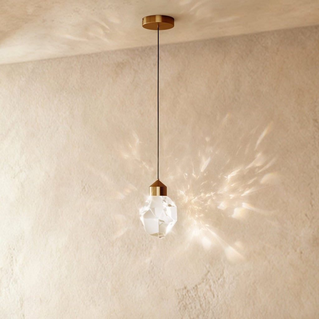 Clérachic gold crystal drop pendant light on a plaster wall, its faceted glass shade casting a wide starburst shadow pattern.