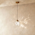 Clérachic gold crystal drop pendant light on a plaster wall, its faceted glass shade casting a wide starburst shadow pattern.