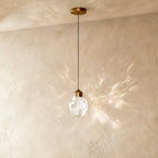 Clérachic gold crystal drop pendant light on a plaster wall, its faceted glass shade casting a wide starburst shadow pattern.