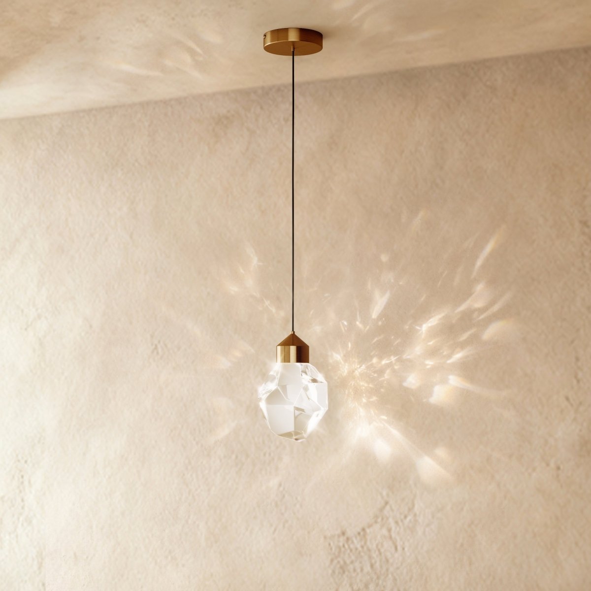 Clérachic gold crystal drop pendant light on a plaster wall, its faceted glass shade casting a wide starburst shadow pattern.