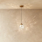 Clérachic crystal drop pendant light with brass mount throws overlapping starburst shadows across a warm plaster wall.