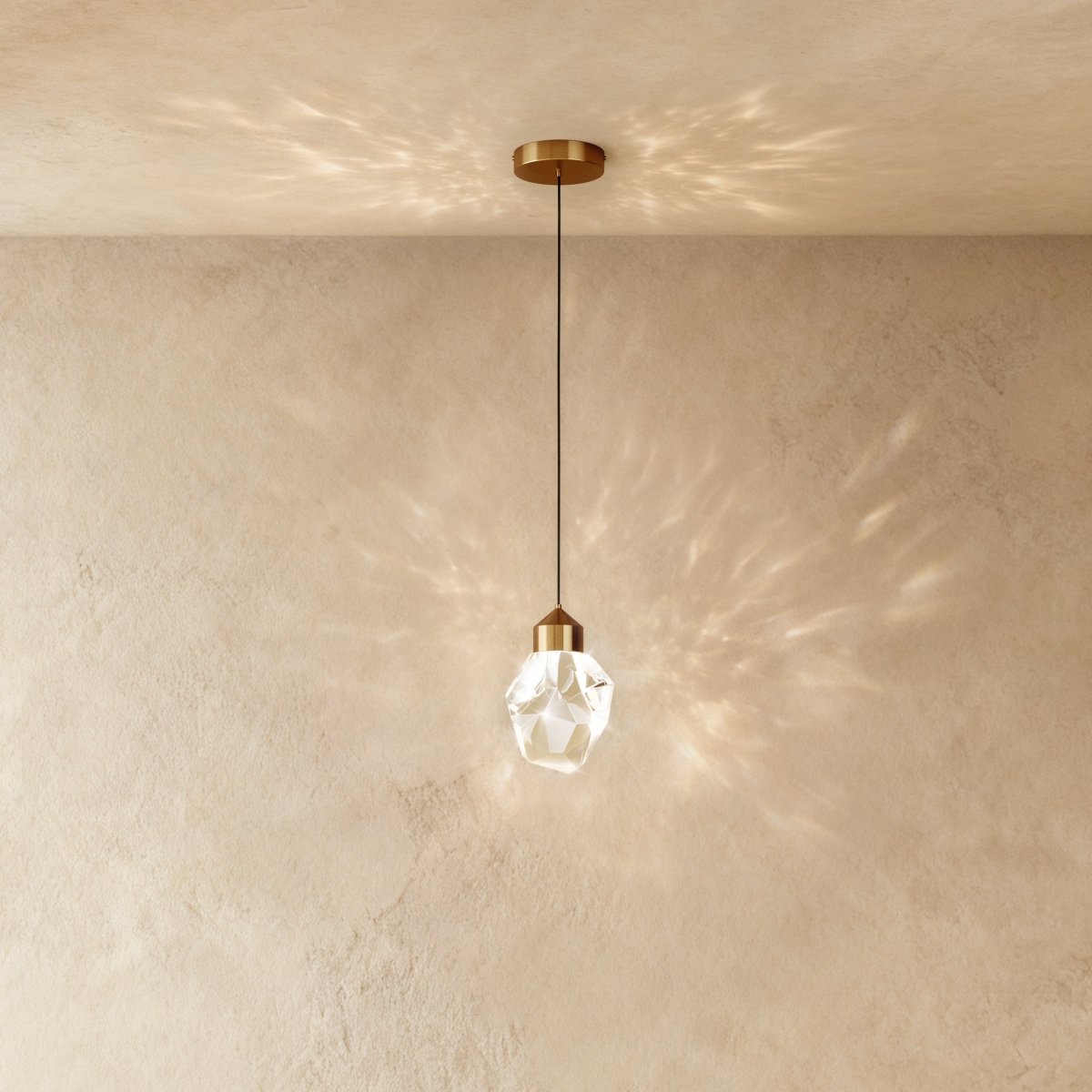 Clérachic crystal drop pendant light with brass mount throws overlapping starburst shadows across a warm plaster wall.