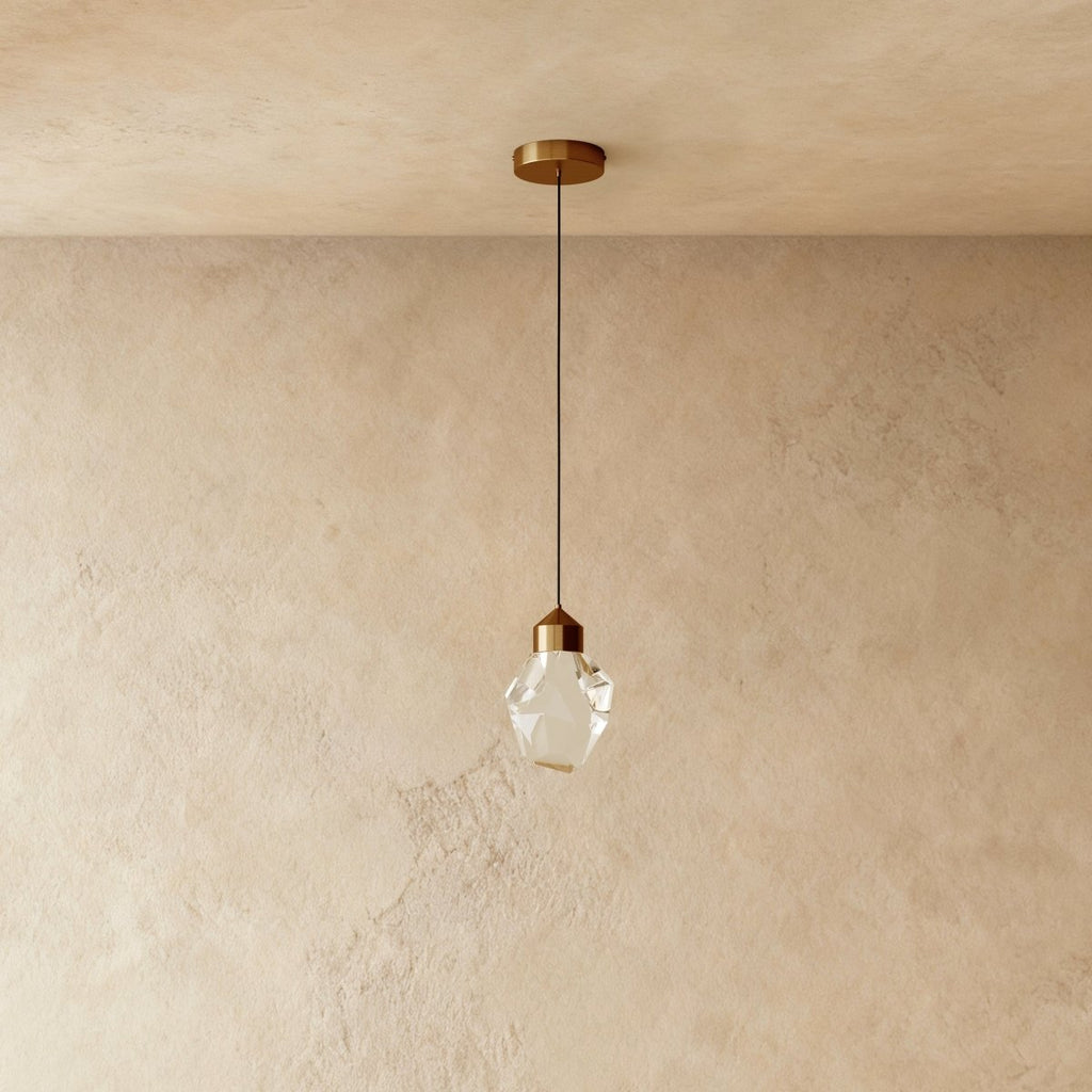 Close view of the Clérachic gold crystal pendant's faceted glass shade and brass cap against a textured plaster wall.