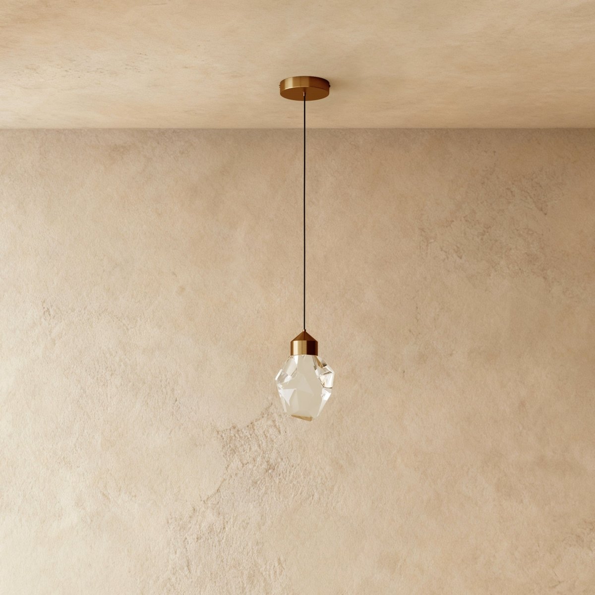 Close view of the Clérachic gold crystal pendant's faceted glass shade and brass cap against a textured plaster wall.