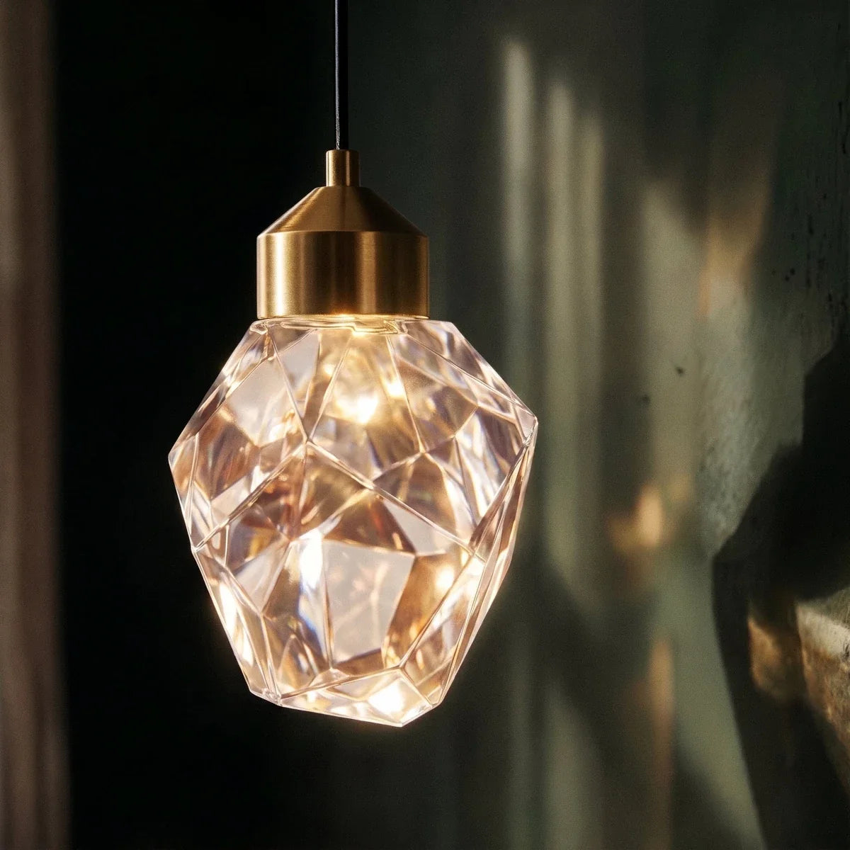 Detail of the Clérachic crystal drop pendant's angular faceted glass shade and brushed brass fitting against a dark backdrop.