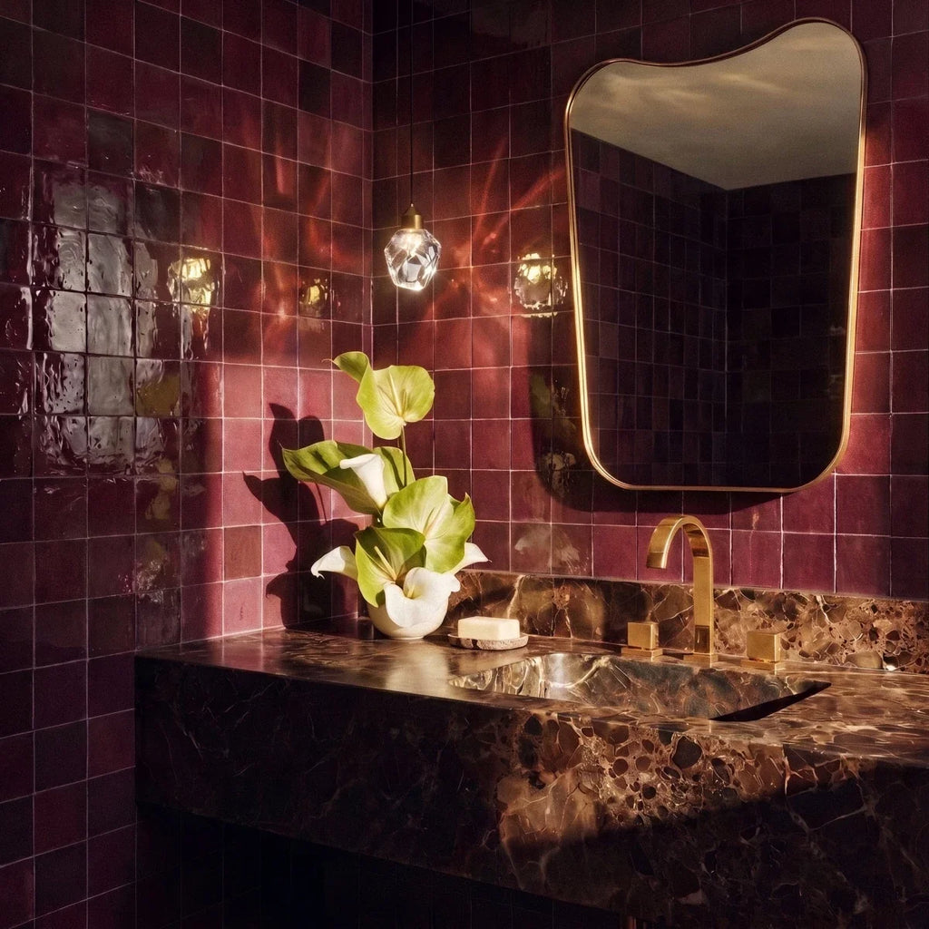 Clérachic crystal drop pendant light lit above a burgundy-tiled bathroom vanity with a brass-framed mirror and marble counter.