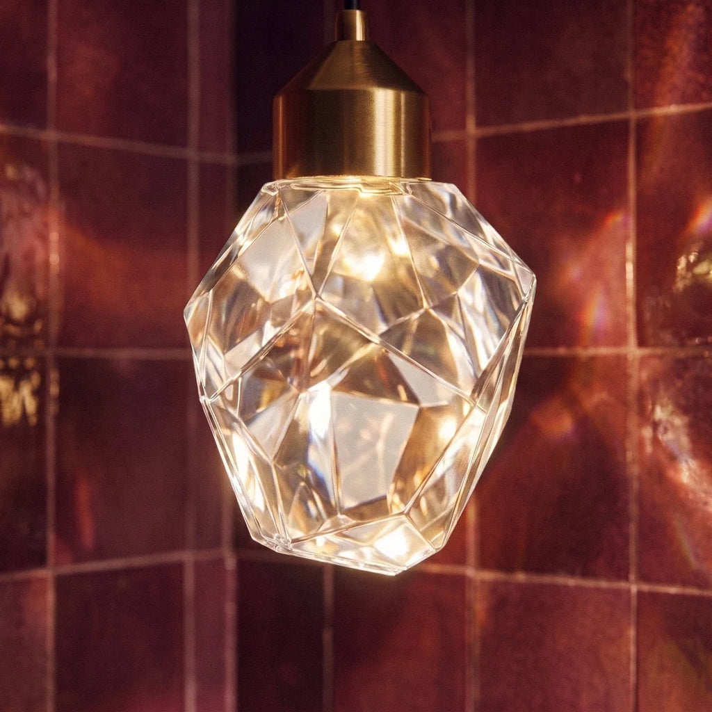 Close-up of the Clérachic crystal drop pendant's faceted glass shade glowing warmly against glossy burgundy tile.