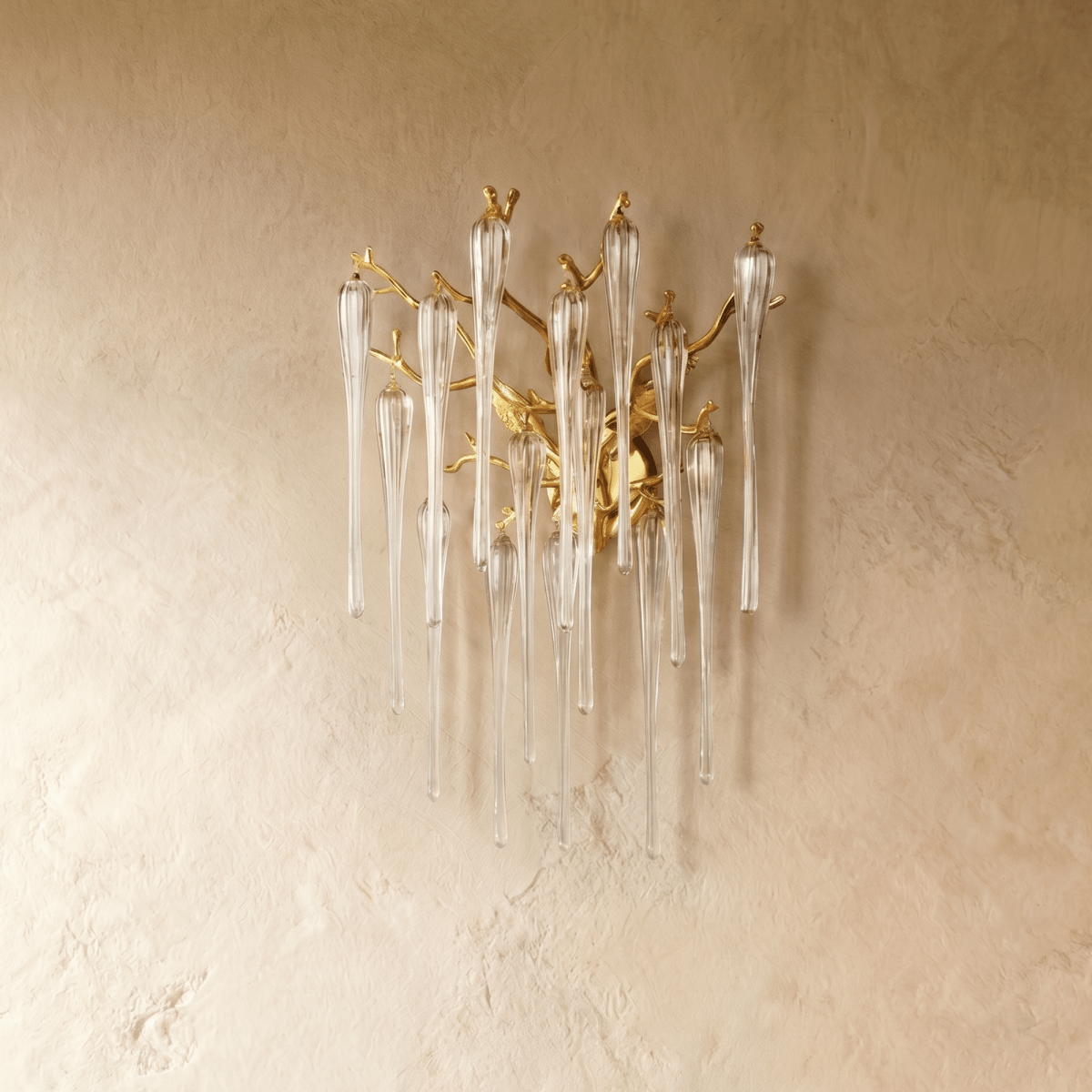 Clérachic gold branch wall lamp with long clear glass icicle drops, switched off against a warm textured plaster wall.