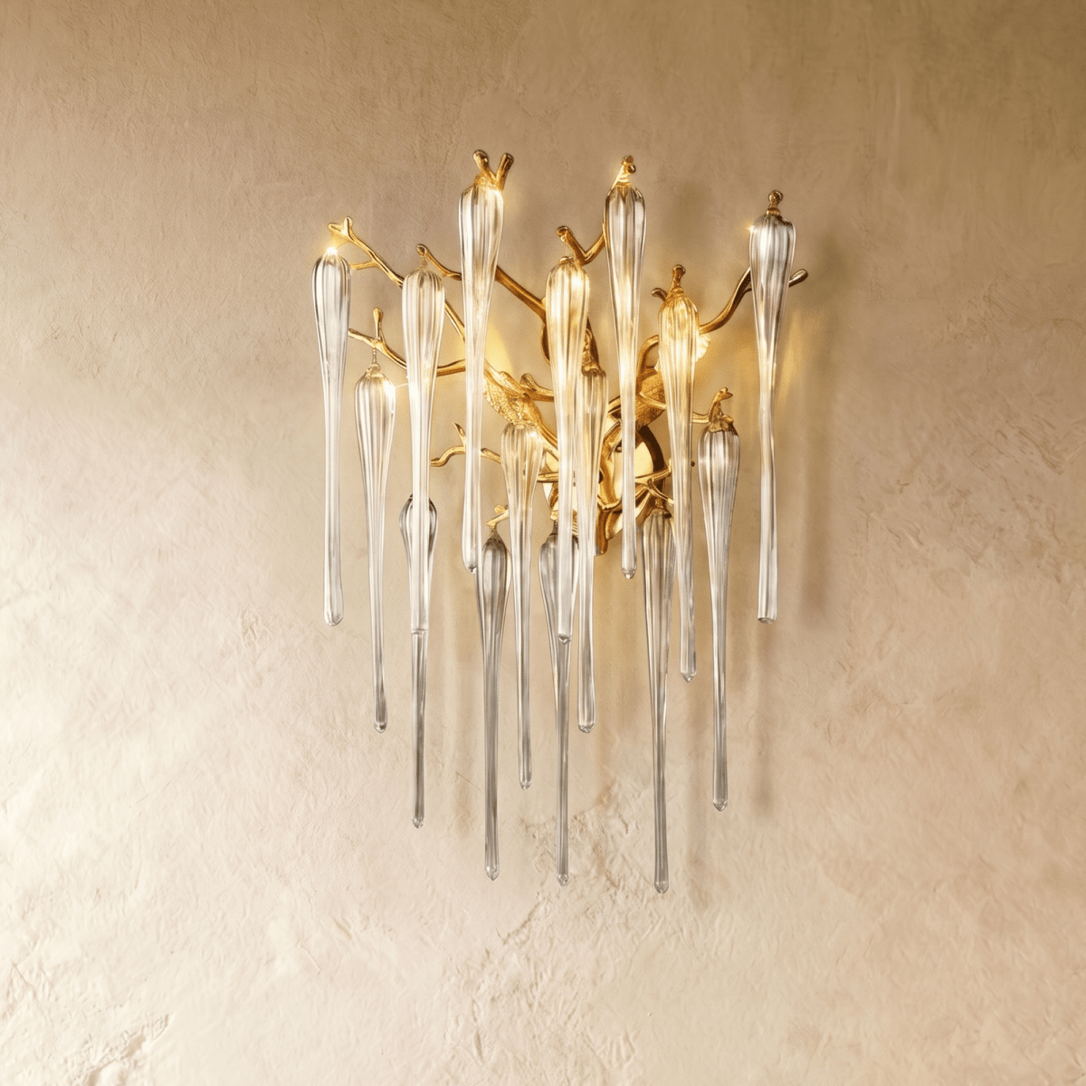 Clérachic gold branch wall lamp with clear fluted glass drops, shown a little larger on a plaster wall in warm light.