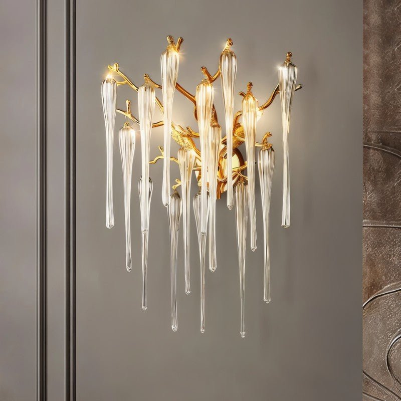 Clérachic gold branch wall lamp with glass drops on a grey panelled wall in a room, a bronze relief panel at the edge.