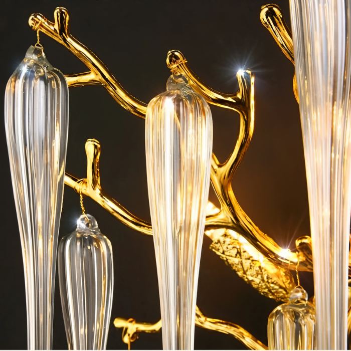 Close up of Clérachic gold branch arms and ribbed clear glass drops with tiny lit bulbs, against a dark studio backdrop.